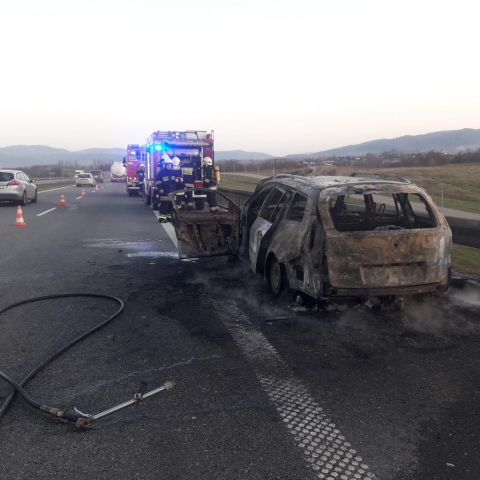 Akcja ugaszania płonącego pojazdu - na zdjęciu samochody strażackie, strażacy oraz doszczętnie spalony samochód